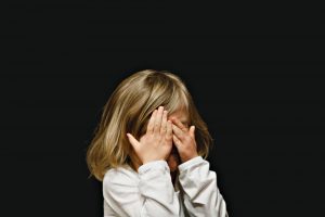 A little girl with hands over her face on a black background
